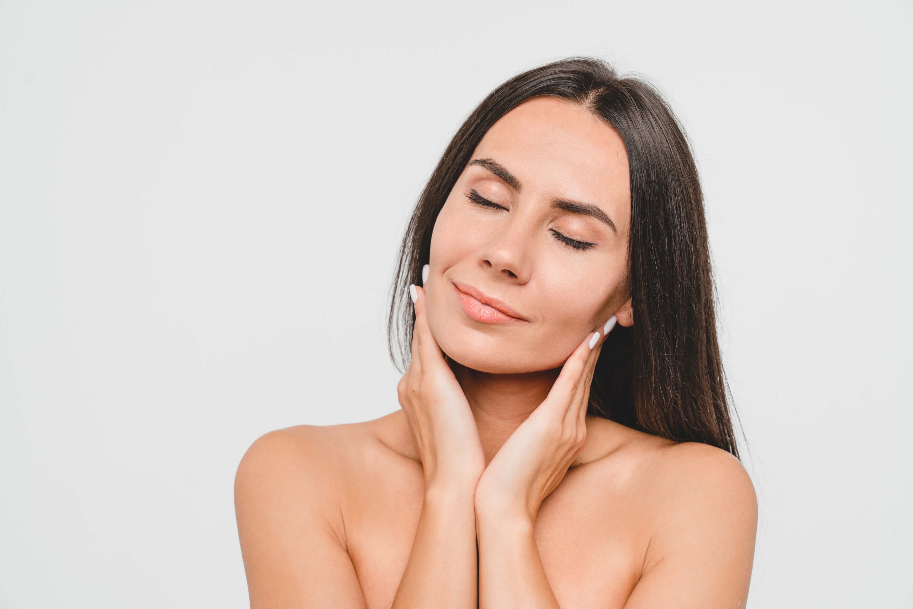 Woman with long dark hair gently touching her face with closed eyes, appearing relaxed.