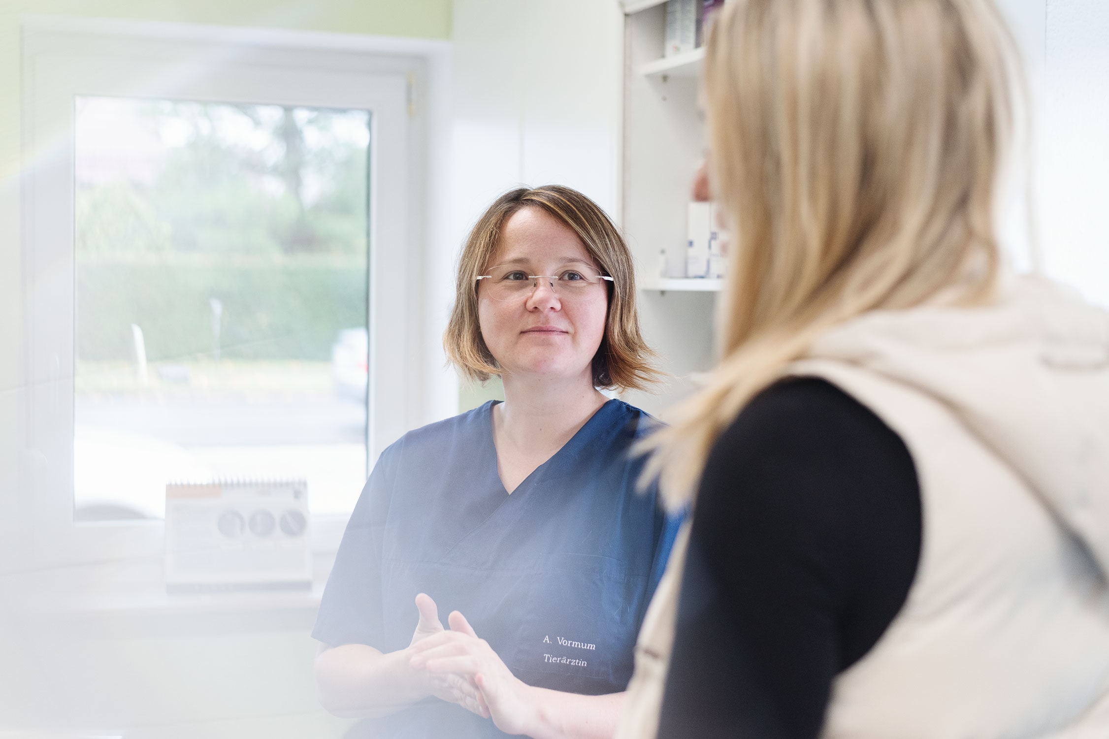 Tierärztin im blauen Kittel berät eine Tierhalterin in der Praxis.