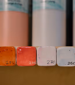 Vier Keramikfarbproben in Orange, Rot, Hellrosa und Weiß mit handgeschriebenen Nummern.