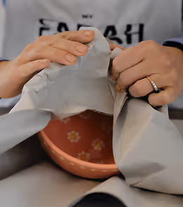 Eine bemalte Keramikschale wird in graues Papier gewickelt.