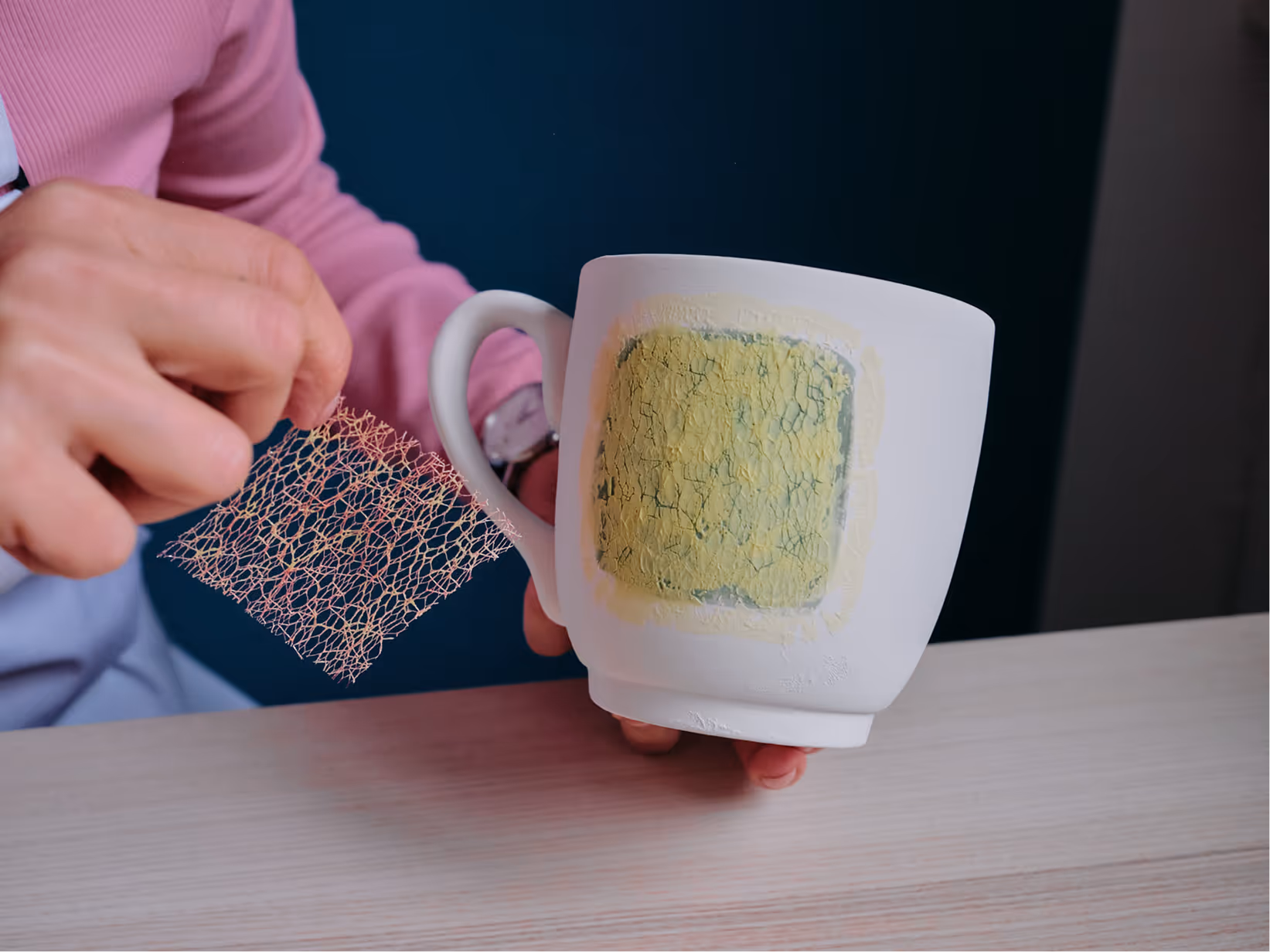 Person hält eine weiße Tasse mit einem trockenen Farbfleck und verwendet eine Mesh-Siebdruckfolie.