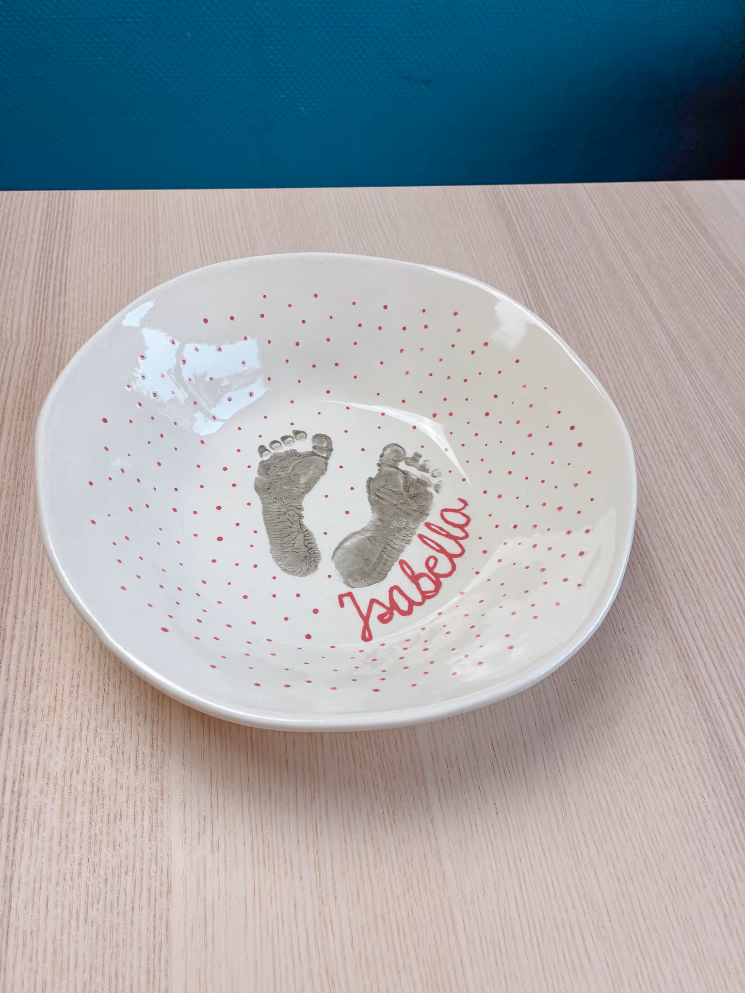 Weißer Keramikteller mit kleinen roten Punkten und Babyfußabdrücken.