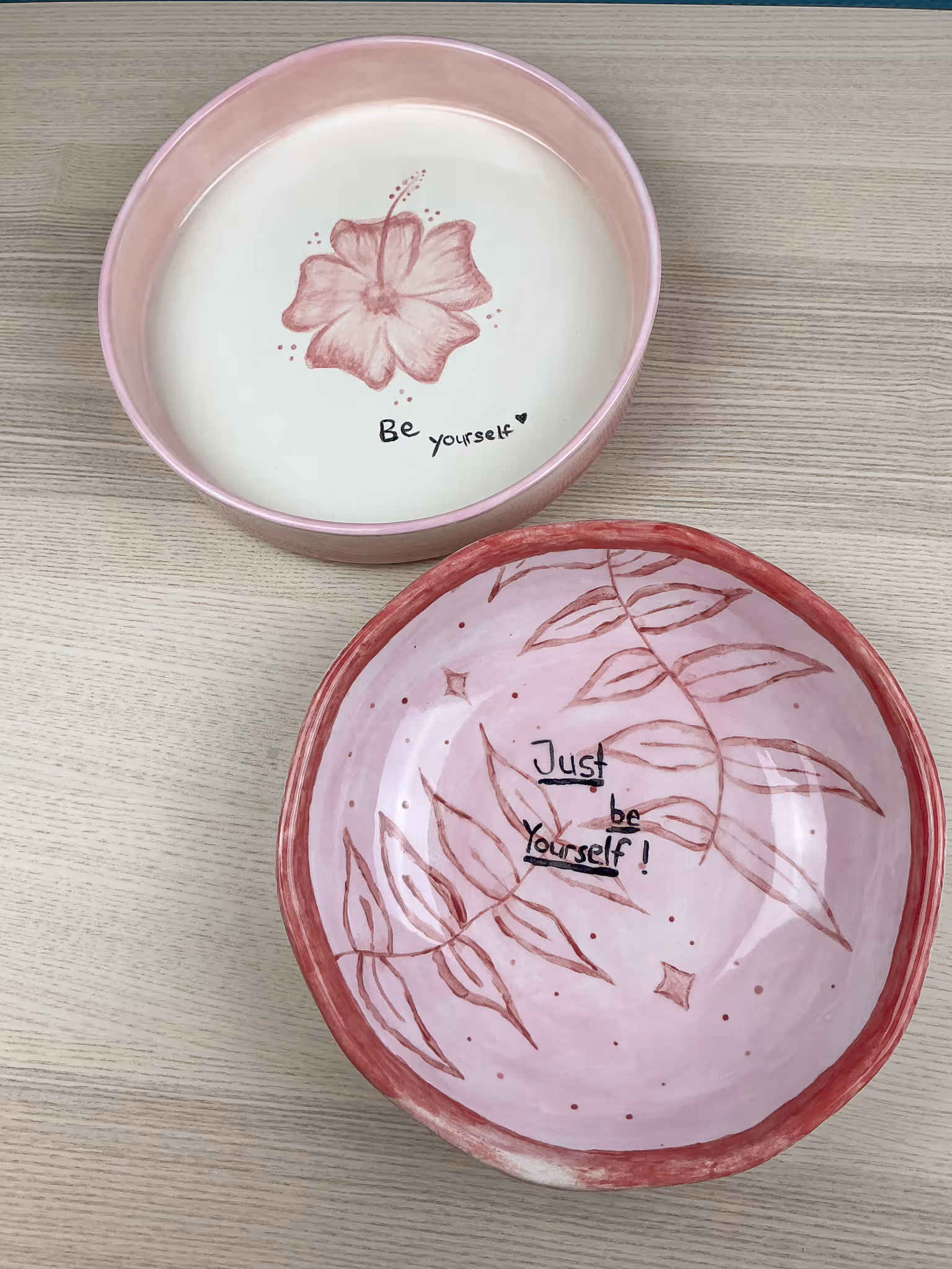 Zwei rosa Keramikschalen mit Blumen- und Blättermotiven und den Schriftzügen ‚Be yourself‘ und ‚Just be Yourself!‘.