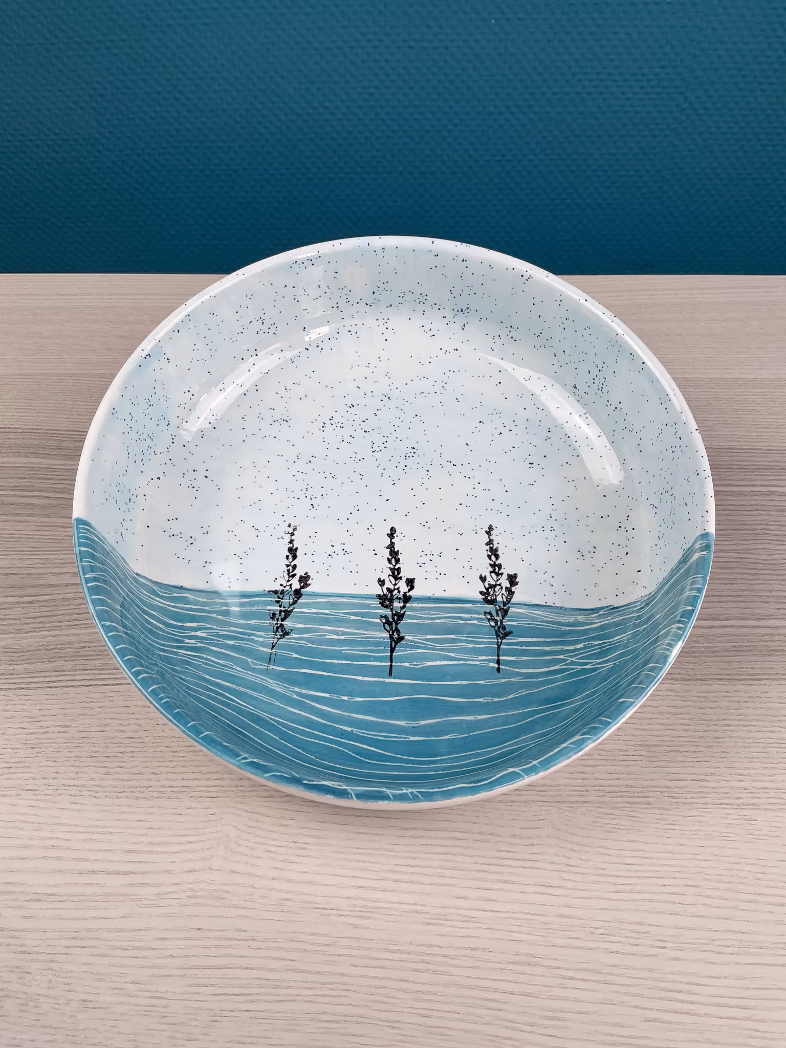 Bemalte Keramikschale mit blauem Wellenmuster und drei schwarzen Pflanzenmotiven.