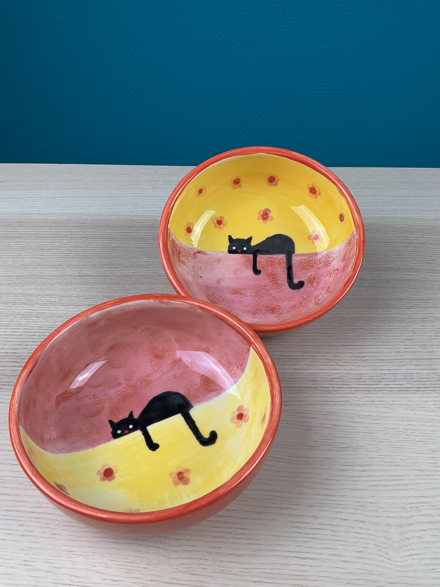 Zwei bunt bemalte Schalen mit schwarzen Katzenmotiven auf gelb-roten Innenflächen.