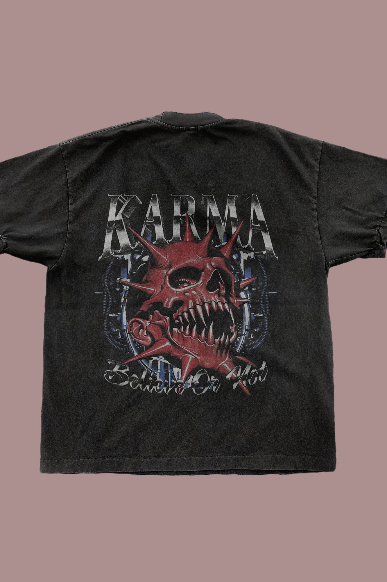 Back view of black t-shirt displaying 'KARMA' text at top in metallic lettering, featuring red demonic skull with spikes and fangs surrounded by crossed weapons or mechanical elements, with 'Believe Or Not' script text at bottom