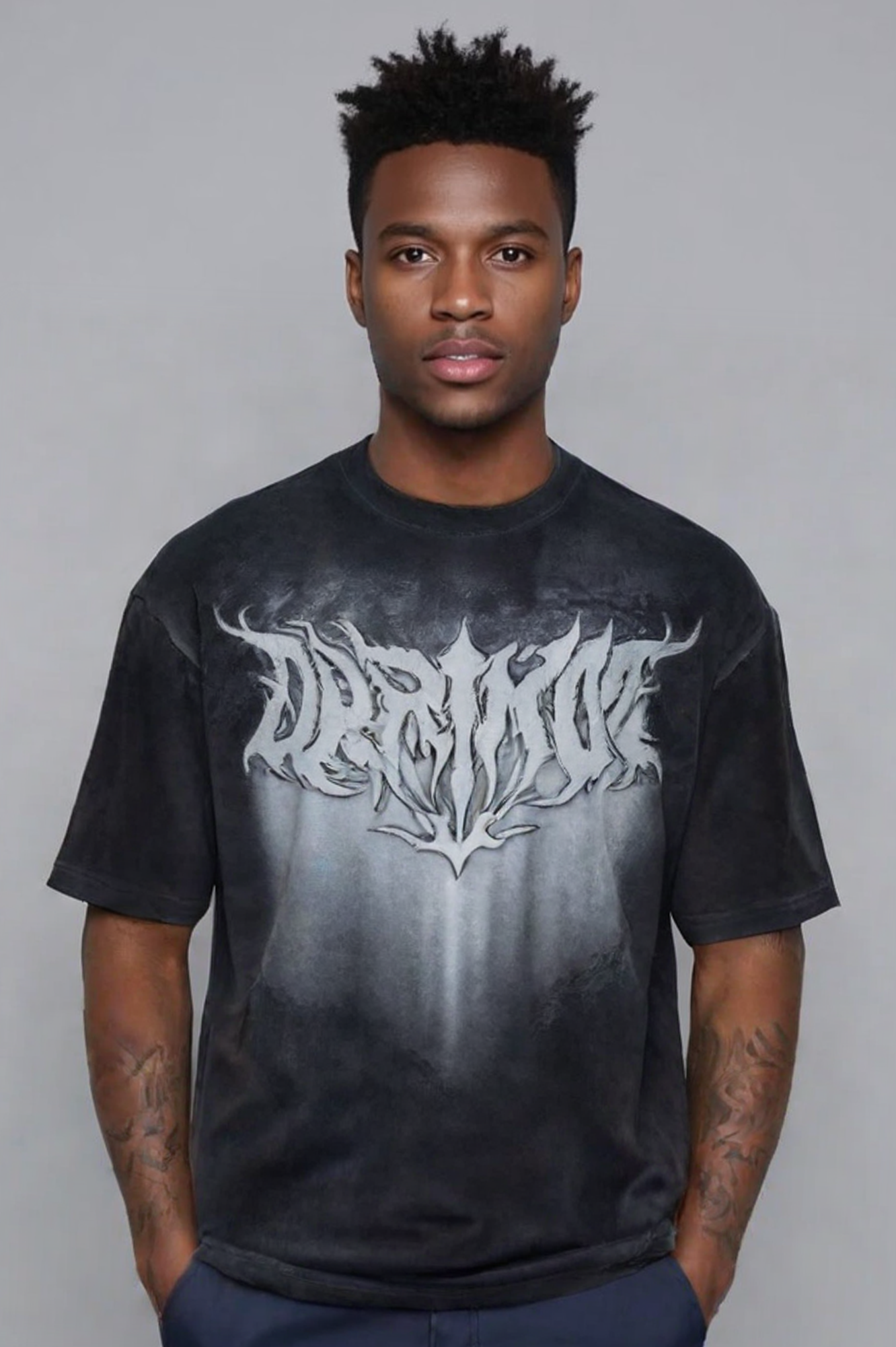 Man wearing a dark tie-dye or gradient t-shirt with white gothic/metal band-style lettering across the chest, standing against a gray background