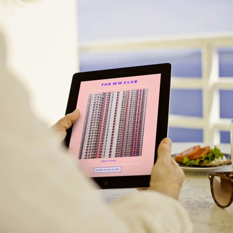 Person reading a colorful email newsletter on a tablet with breakfast, sunglasses, and coffee on a table.