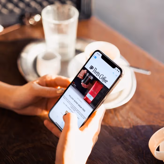 Person holding smartphone displaying a Peet's Coffee email template Holiday Blend Sneak Peek, coffee cup blurred in the background.