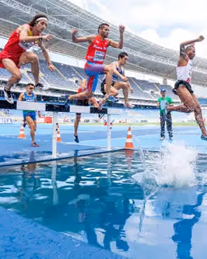 Track and field athletes mid-jump over water hurdle in stadium, symbolizing Olympic-themed email design with action, energy, and global spirit.