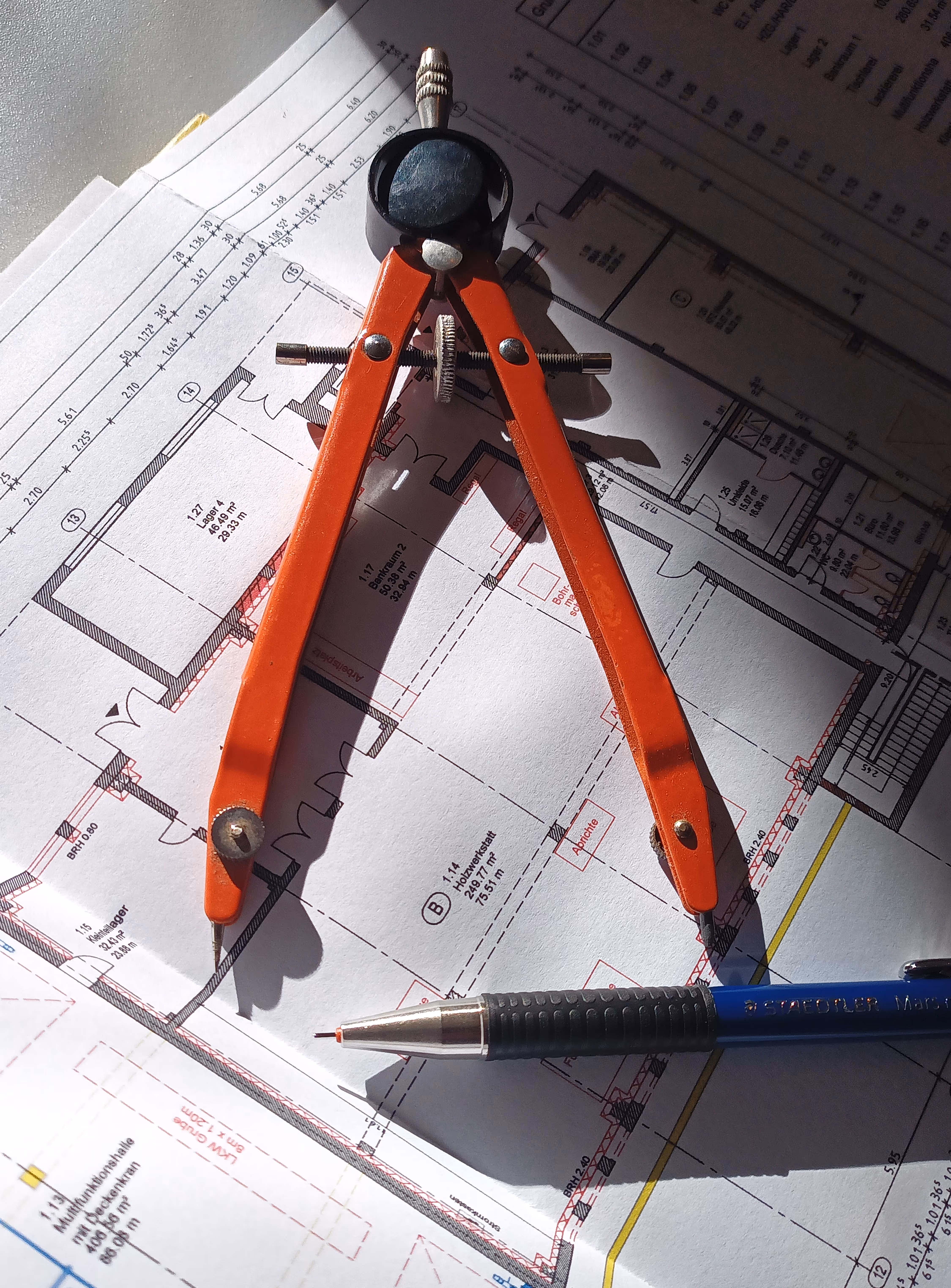 Ein Zirkel und ein Stift liegen auf einem Bauplan.