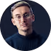 Mann mit Brille und blauem Pullover vor dunklem Hintergrund.
