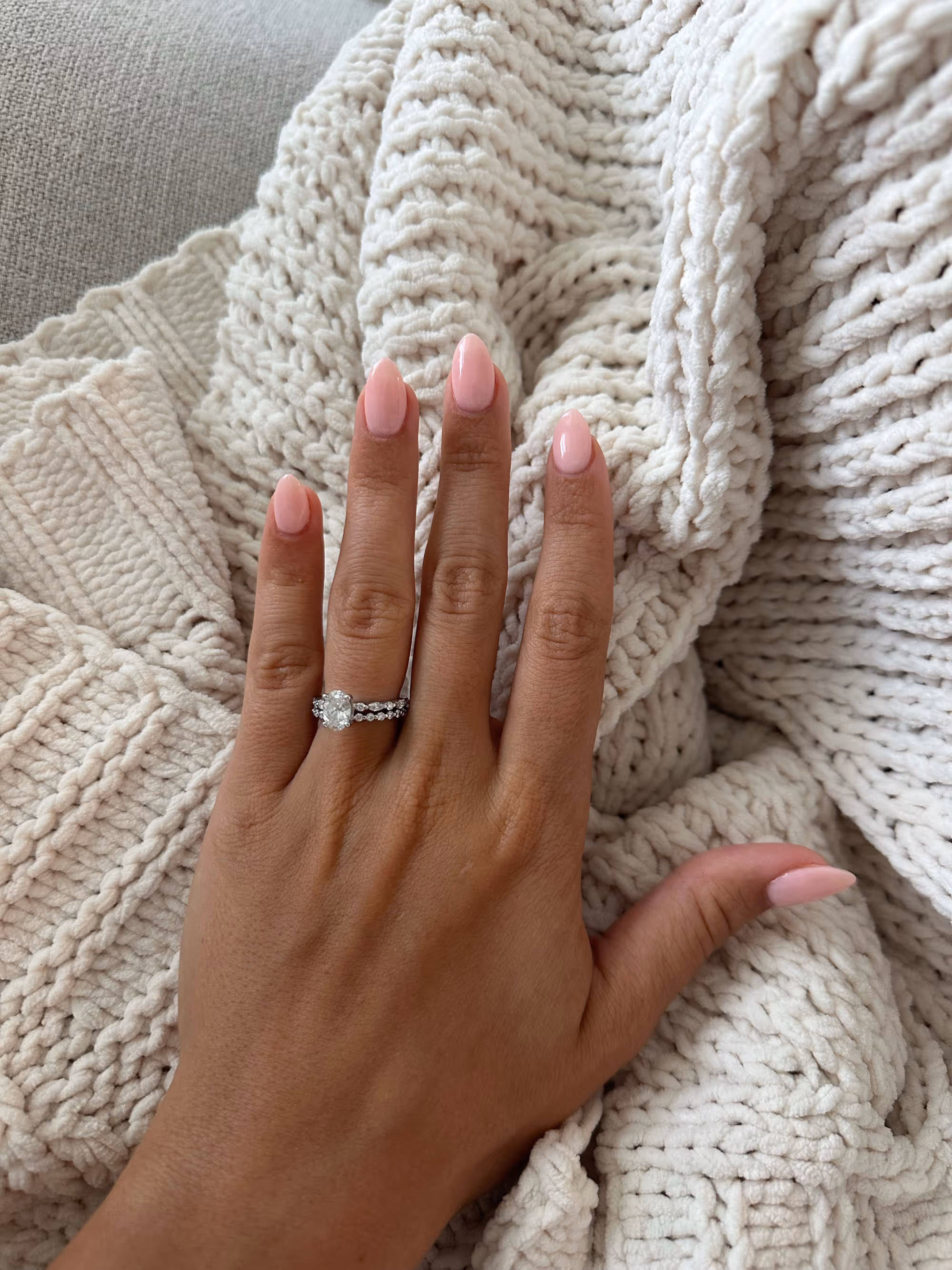 Hand with light pink nails and rings on cozy blanket