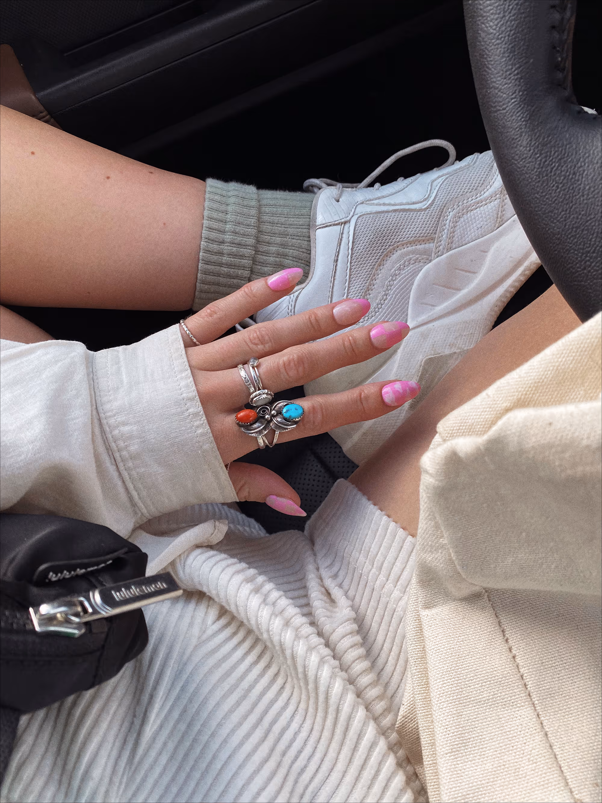 Hand with pink swirl nails and rings in car