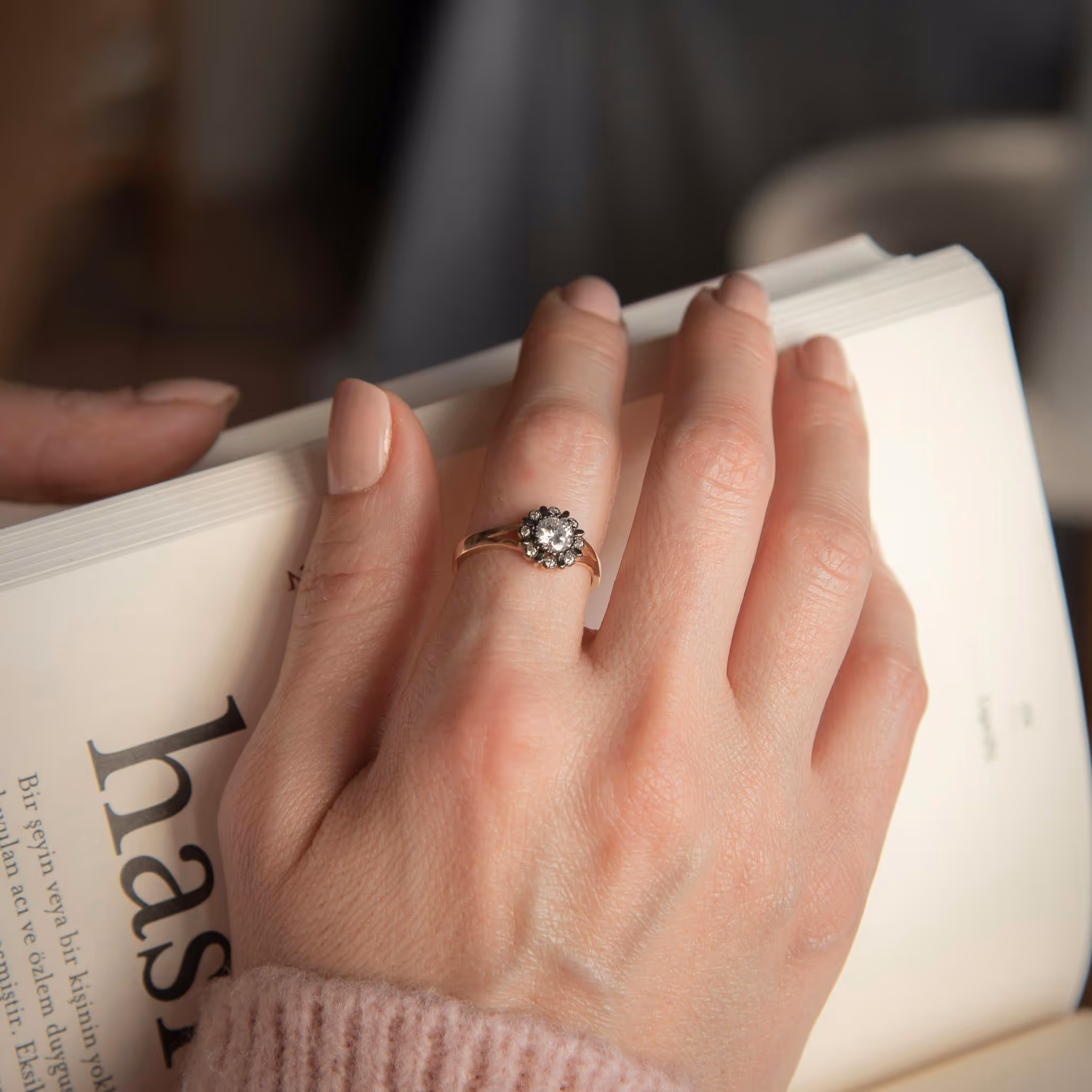 Hand with nude nails wearing a diamond ring, holding a book
