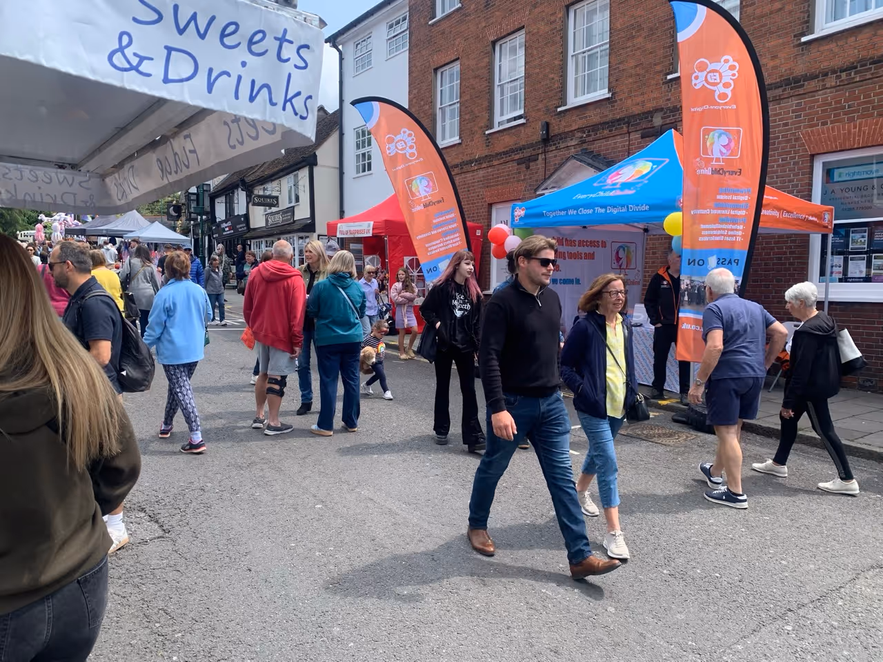 People walking and browsing booths at an outdoor street fair with colorful tents and banners under a partly cloudy sky.