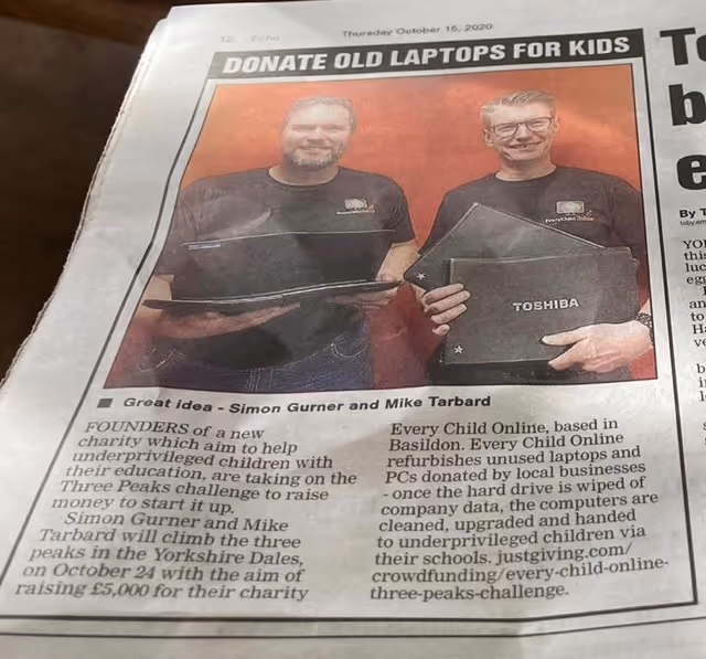Newspaper clipping showing Simon Gurner and Mike Tarbard holding laptops for a charity drive to donate old laptops to underprivileged children.