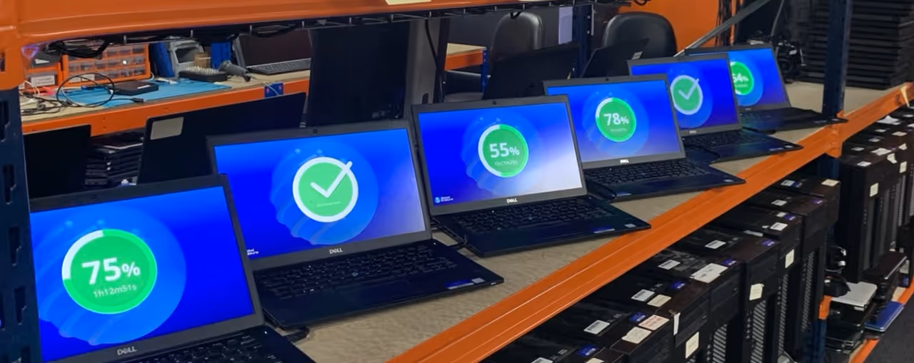 Row of Dell laptops on an orange metal shelf displaying various battery charge levels and check marks on their blue screens.