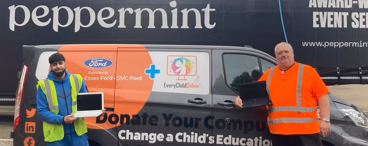Two men in safety vests holding laptops stand in front of a van with a 'Donate Your Computer' sign supporting Essex Ford and Every Child Online.