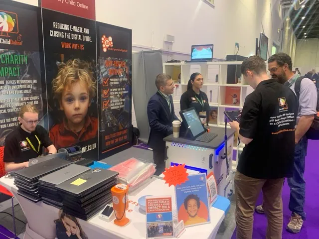 Exhibition booth promoting digital reuse and e-waste reduction with stacked laptops, informational signs, and several people interacting at a tech event.