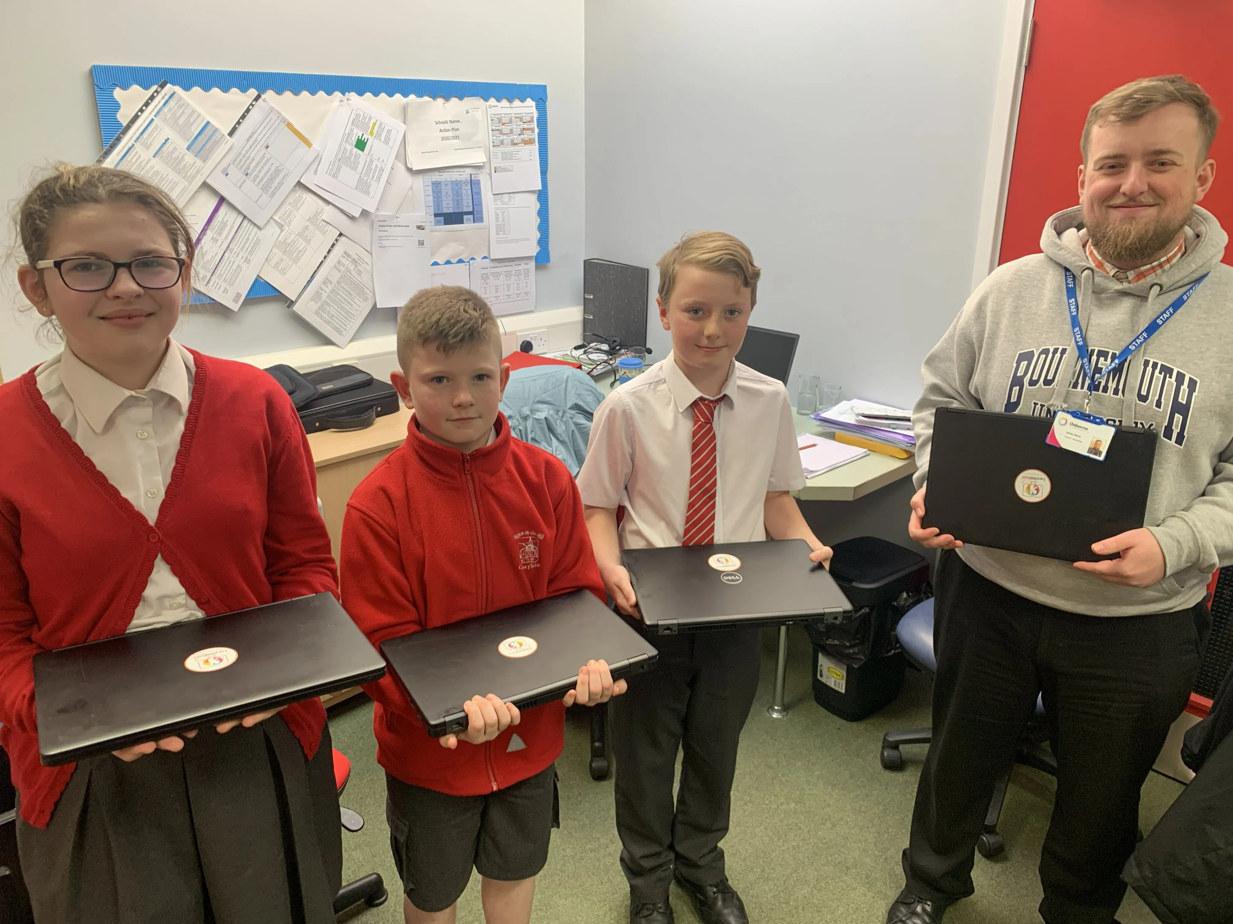 Three students and a teacher holding closed laptops with stickers in a classroom.