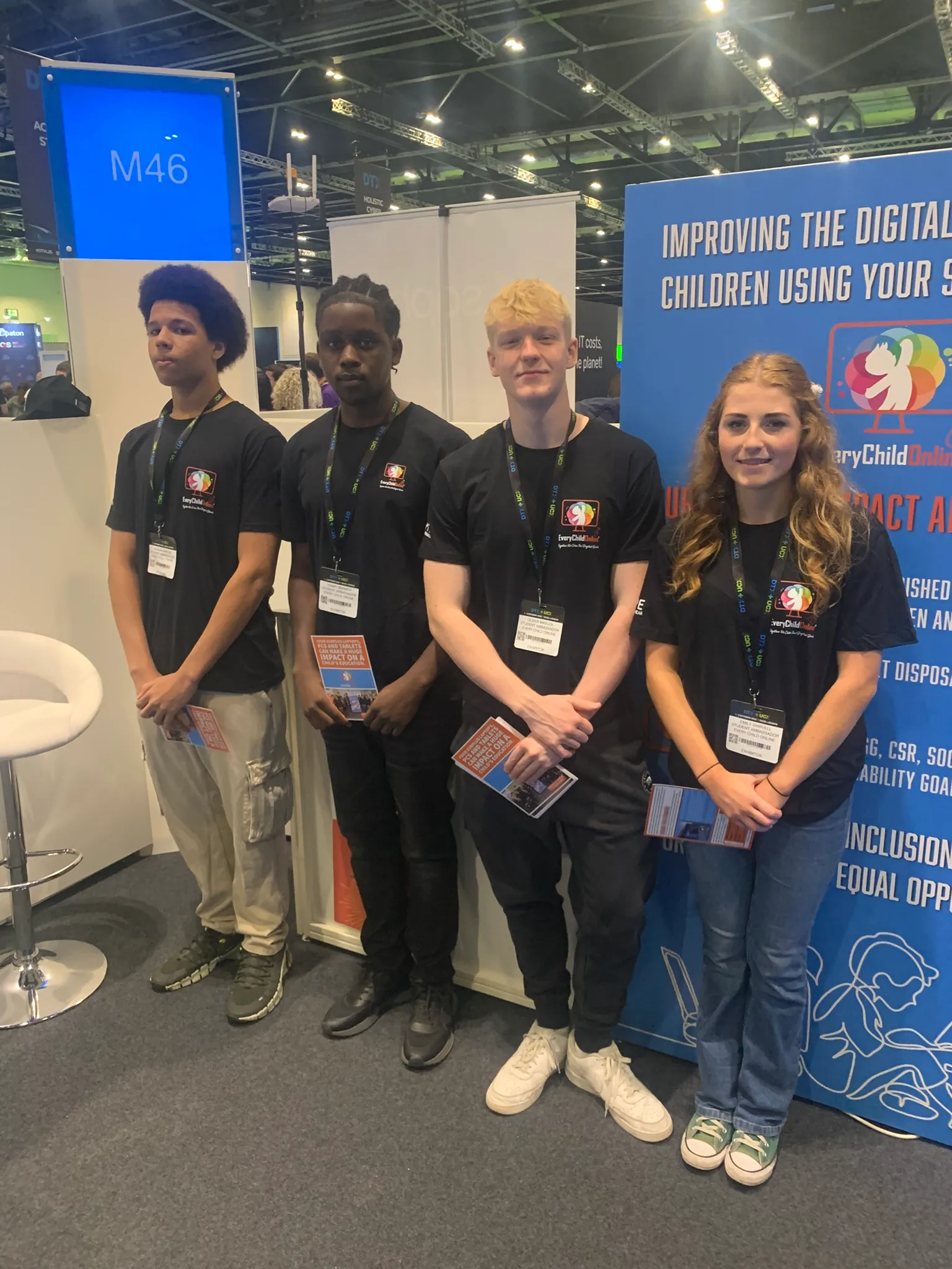 Four young people wearing matching black Every Child Online shirts holding brochures at a convention booth.