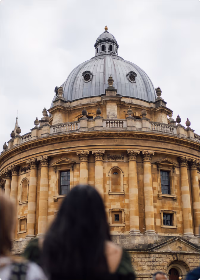 People standing in front of the Radcliffe Camera, a historic circular building with a large dome in Oxford, England.