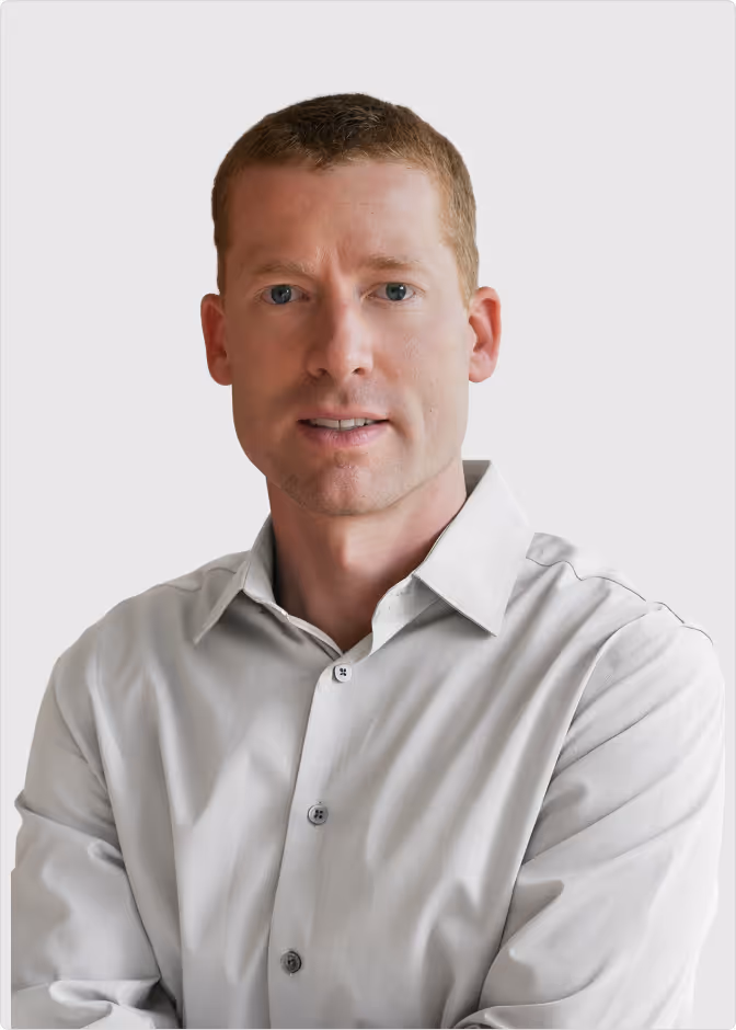 Portrait of a man with short light brown hair wearing a light gray button-up shirt against a plain light background.