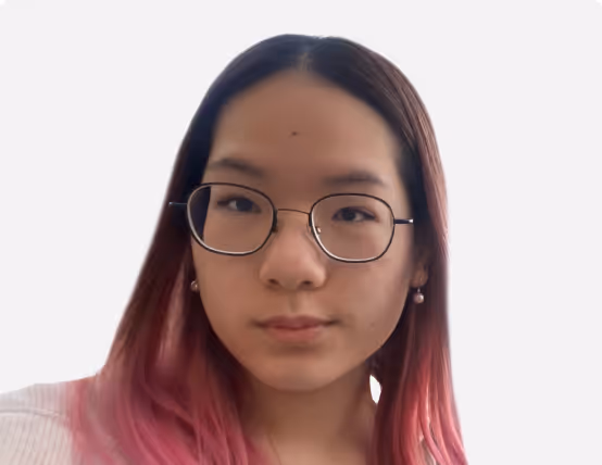 Young woman with long dark hair dyed pink at the ends, wearing glasses and pearl earrings, against a plain white background.