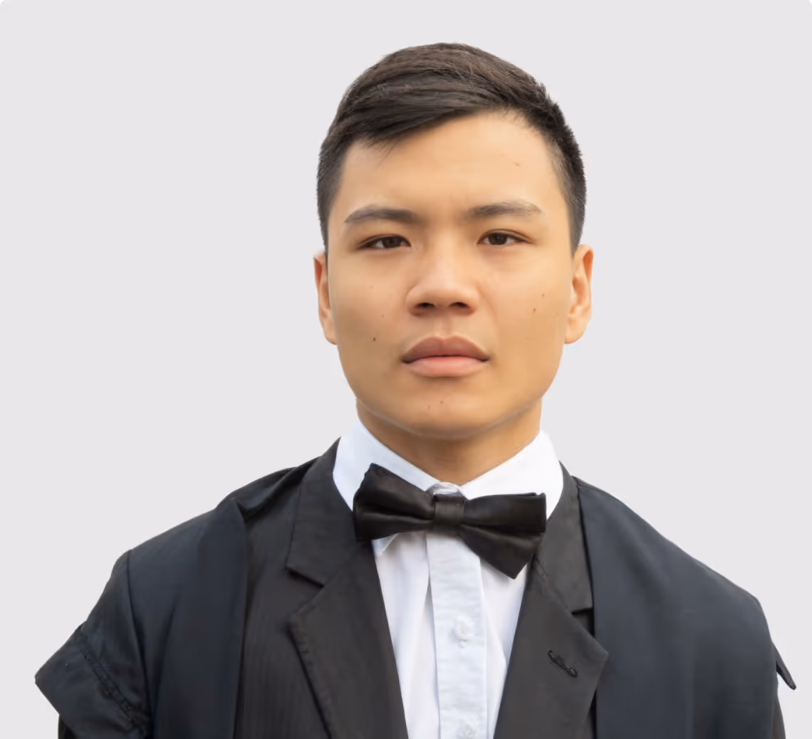 Young man wearing a black tuxedo jacket, white shirt, and black bow tie against a plain light background.