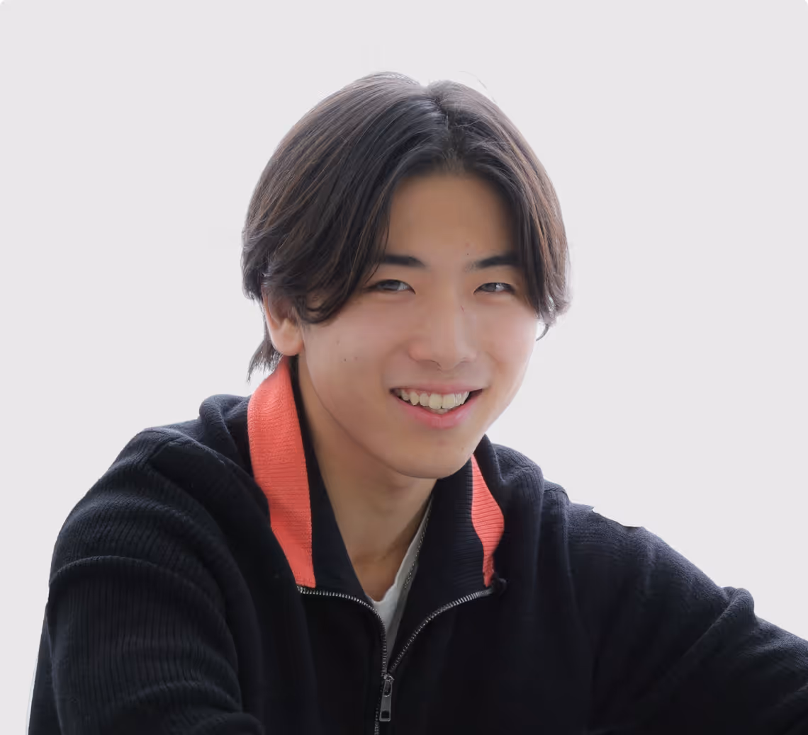 Smiling young man with black hair wearing a black jacket with an orange collar.