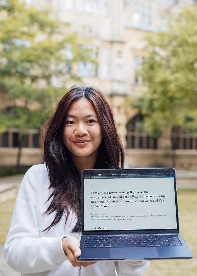 Woman outdoors holding a laptop displaying a research paper titled "How assistive governmental policy shapes the entrepreneurial landscape and affects the success of startup businesses."