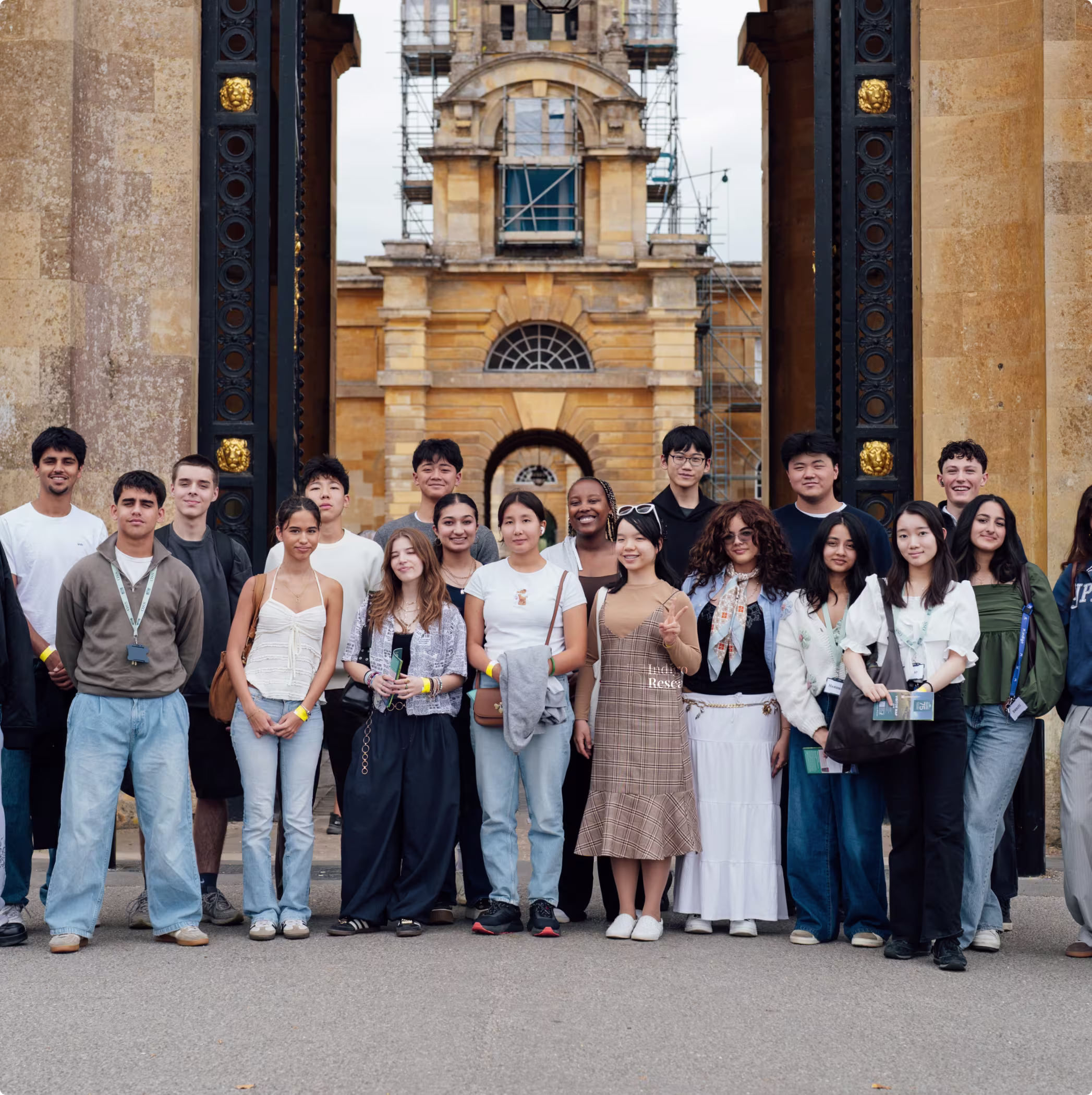 Group of diverse young adults standing in front of a historical stone archway with ornate black and gold pillars.