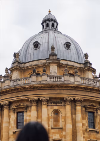 Dome of a historic stone building with classical columns and circular windows under an overcast sky.
