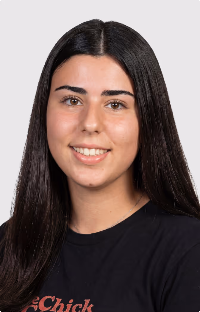 Portrait of a young woman with long dark hair and brown eyes smiling against a plain light background.