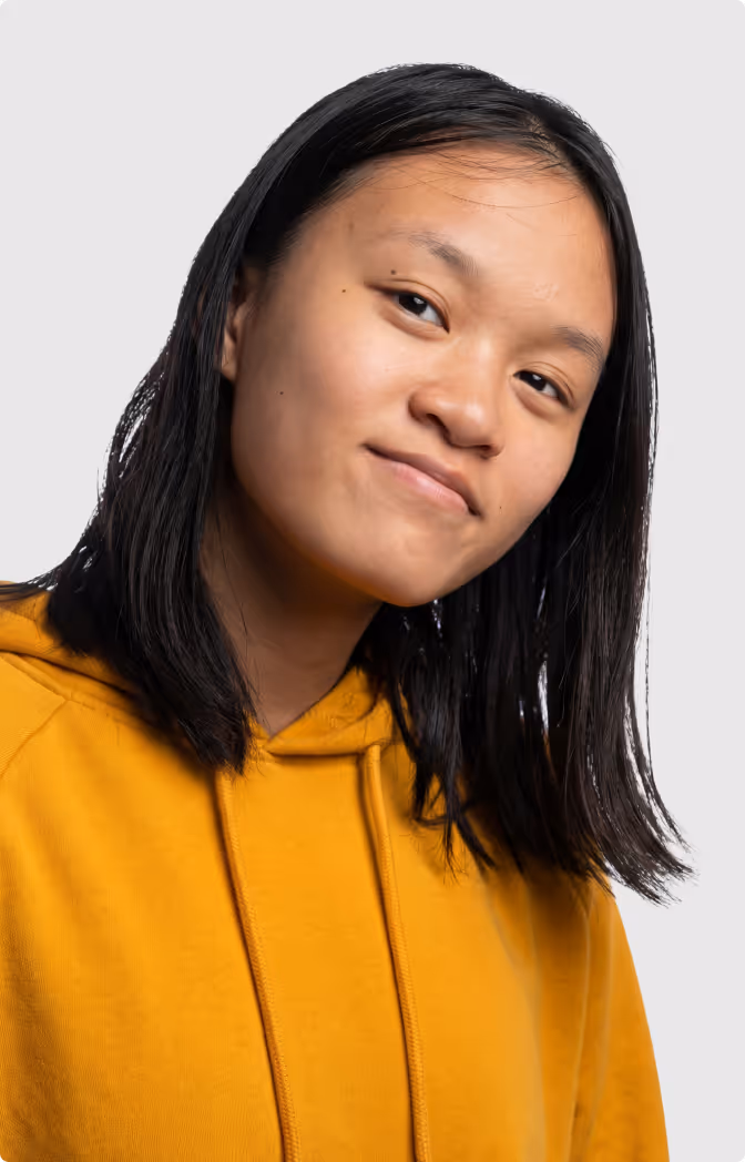 Young woman with shoulder-length black hair wearing a mustard yellow hoodie smiling slightly.