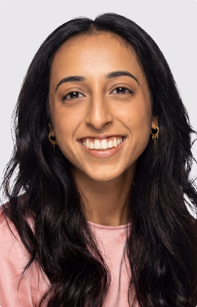 Smiling woman with long black hair wearing gold hoop earrings and a pink top.