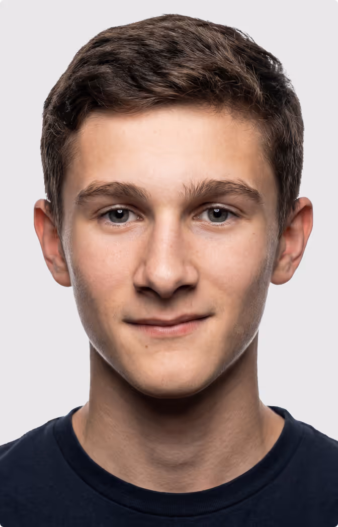 Portrait of a young man with short brown hair wearing a dark shirt, against a plain light background.
