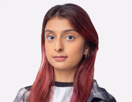 Portrait of a young woman with long reddish hair wearing a plaid shirt over a white top against a plain background.
