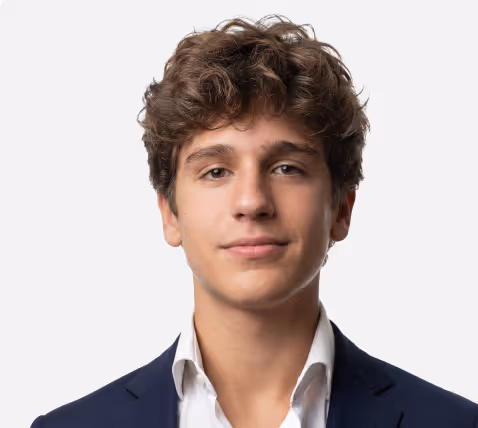 Young man with curly hair wearing a navy blazer and white shirt looking at the camera.