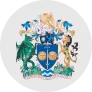 Coat of arms with a shield featuring two golden shells and a white flower, topped with a sea shell, flanked by two lions and tropical plants.