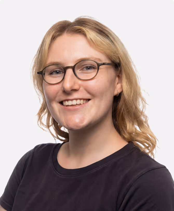 Smiling woman with blonde hair, glasses, and a black shirt against a white background.