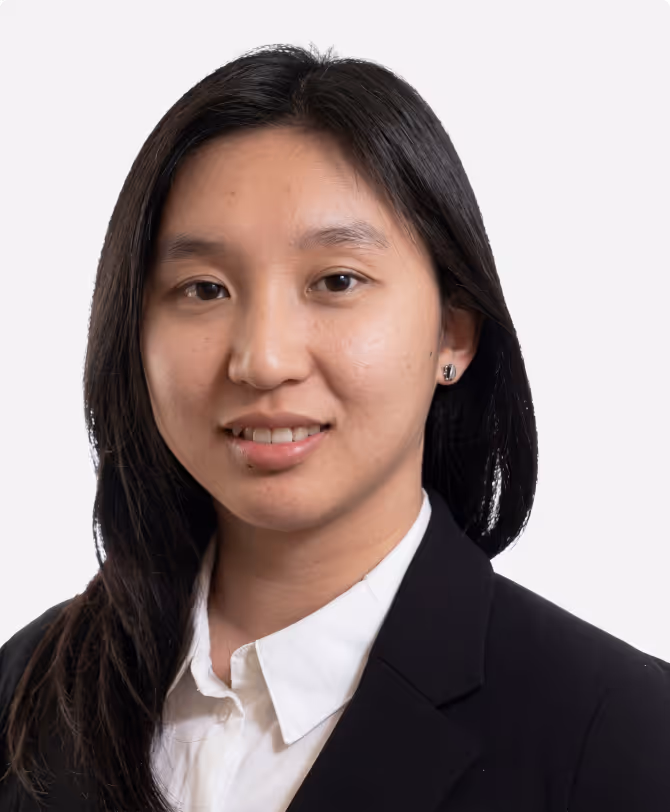 Portrait of a woman with long dark hair wearing a white shirt and black blazer, smiling slightly against a plain background.