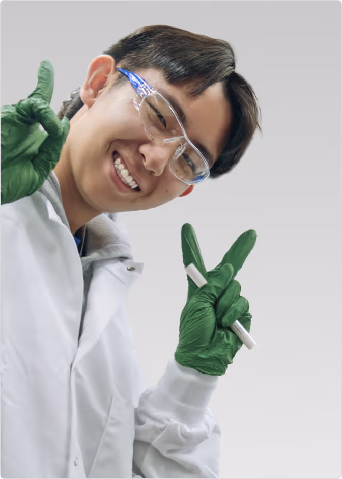 Three scientists wearing lab coats, safety glasses, and gloves working together with lab equipment; one holds a test tube and shows a peace sign.