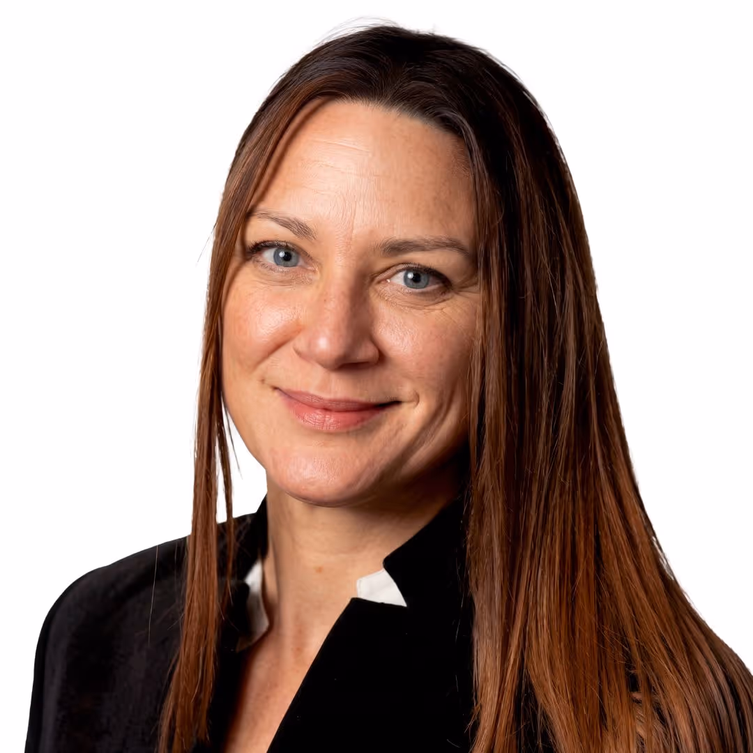 Woman with long brown hair and blue eyes smiling, wearing a black jacket over a white top.