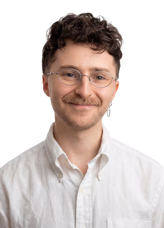 Smiling man with curly hair, glasses, mustache, and white button-up shirt on black background.