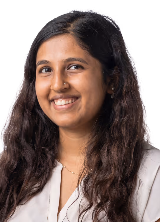 Smiling woman with long dark hair wearing a white blouse and a nose ring.