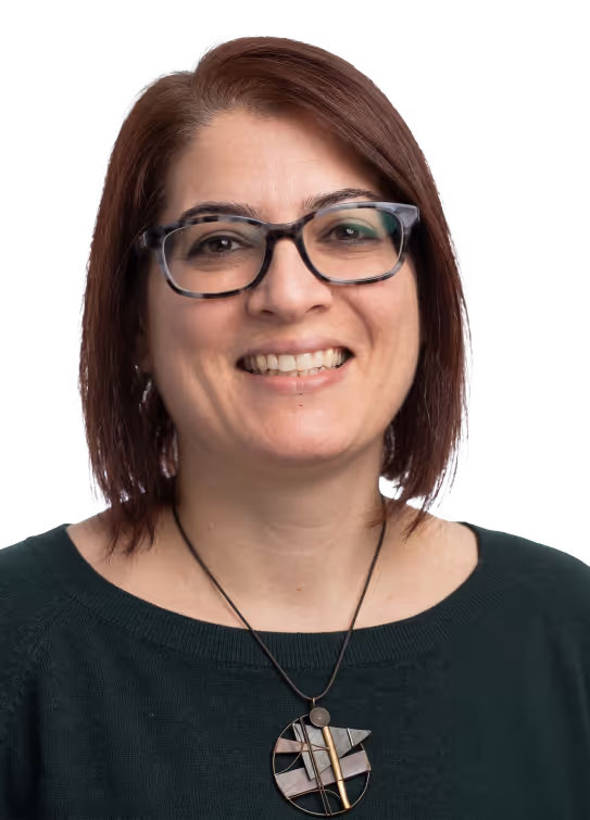 Smiling woman with short brown hair, glasses, dark green top, and modern circular pendant necklace.