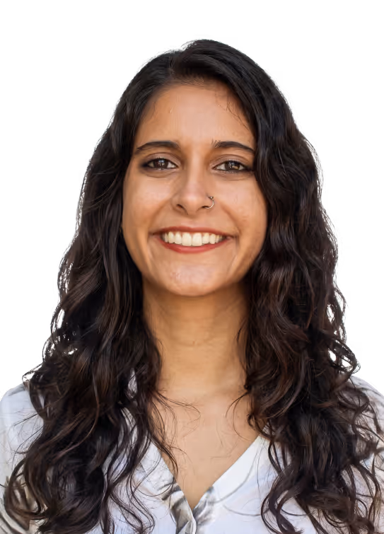 Smiling woman with long curly dark hair and a nose ring wearing a white top.