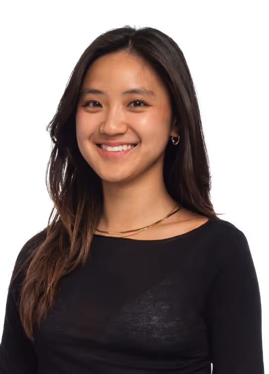 Smiling young woman with long dark hair wearing a black top and gold necklace on a transparent background.